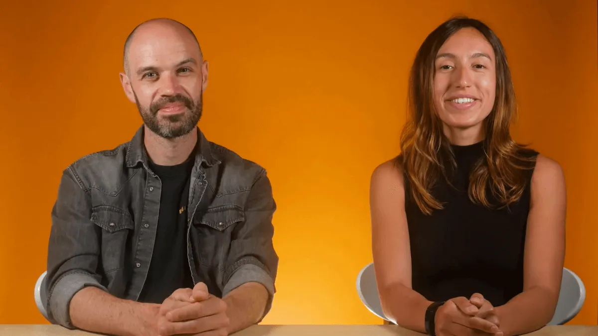 Two members of the OnePageCRM marketing team seated at a table against an orange wall