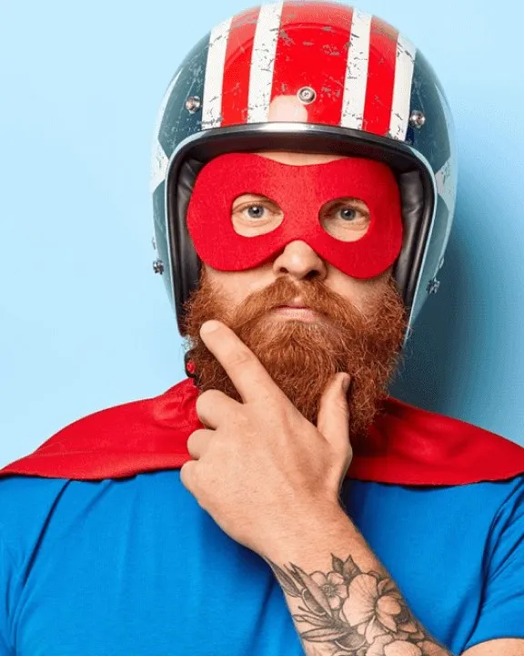 A person in a superhero cape, helmet and eye mask, hand on chin, thinking
