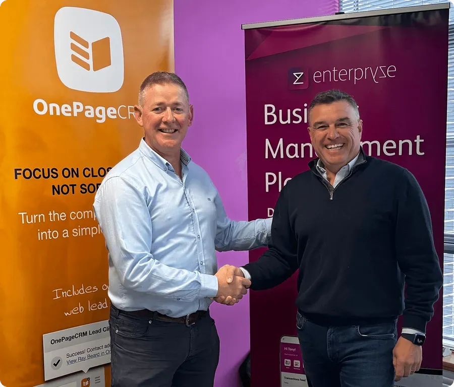 Michael FitzGerald shaking hands in front of OnePageCRM and Enterpryze banners